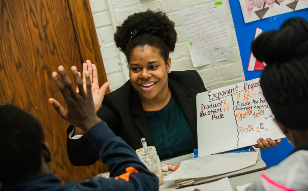 A tutor high fives a student while holding a small whiteboard