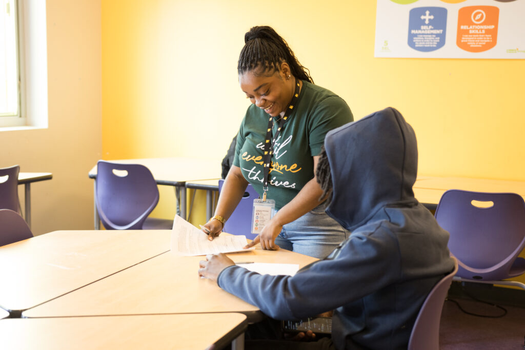 Women mentor works with a teen boy in a classroom