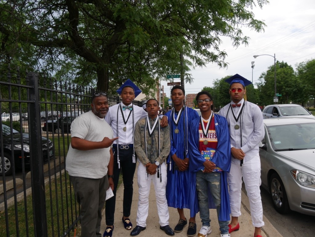 A family faces the camera after a graduation with multiple people in gowns, wearing caps, and have medals and academic cords hanging on their necks