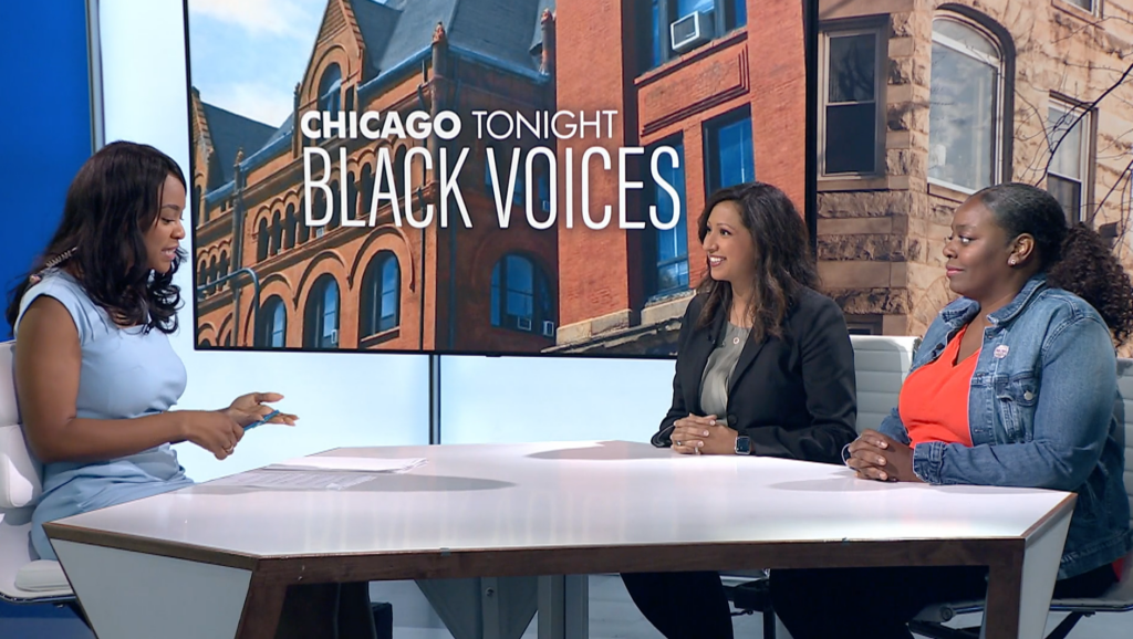 3 woman (including Dr. Bhatt) sitting at a table in front of a screen with the logo "Chicago Tonight Black Voices" on it